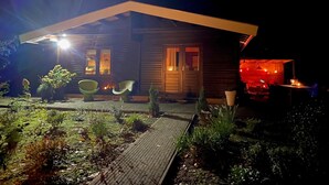 Una casa de madera con un porche cubierto, dos sillas y un pequeño jardín.