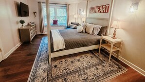 Quarto com cama de dossel, mesa de cabeceira, televisão na parede e janela com cortinas.