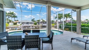 Un espace extérieur abrité, doté d’une piscine, de meubles en osier et offrant une vue sur les palmiers et les maisons.