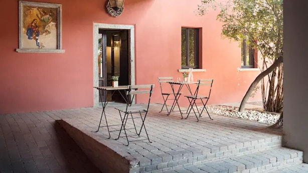 Un patio al aire libre con suelo de ladrillo, una mesa con sillas, un farol colgante y una puerta que da a un espacio interior.