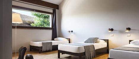 A modern bedroom with two single beds, a standing lamp, and a large window with a view of greenery.