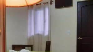 A hotel room with a bed, a desk, a chair, a lamp, a TV on the wall, and a door. - Posada Maya  (Antigua Guatemala)