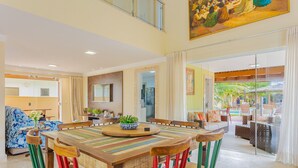 Un comedor amplio con una gran mesa de madera y sillas coloridas, una planta en maceta y vistas del patio exterior.