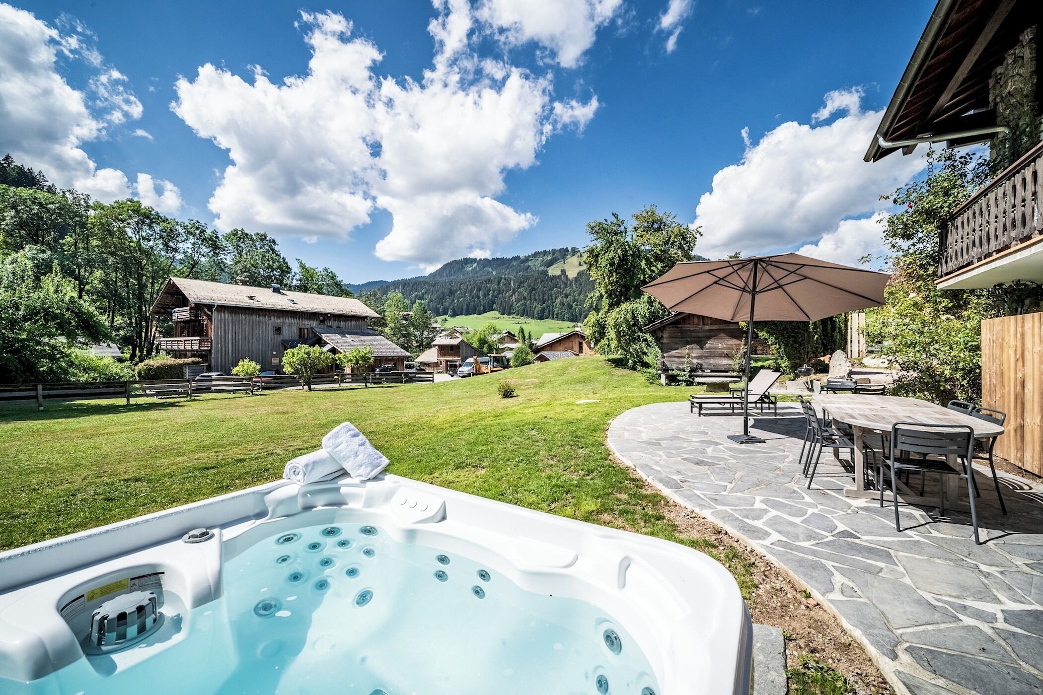 A hot tub in a backyard with a stone patio and outdoor furniture.
