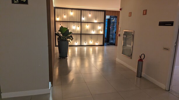 A modern hotel lobby with a large potted plant, a fire extinguisher, and a sign indicating the location of the lavatory. - Sunflower Stays (São Paulo)