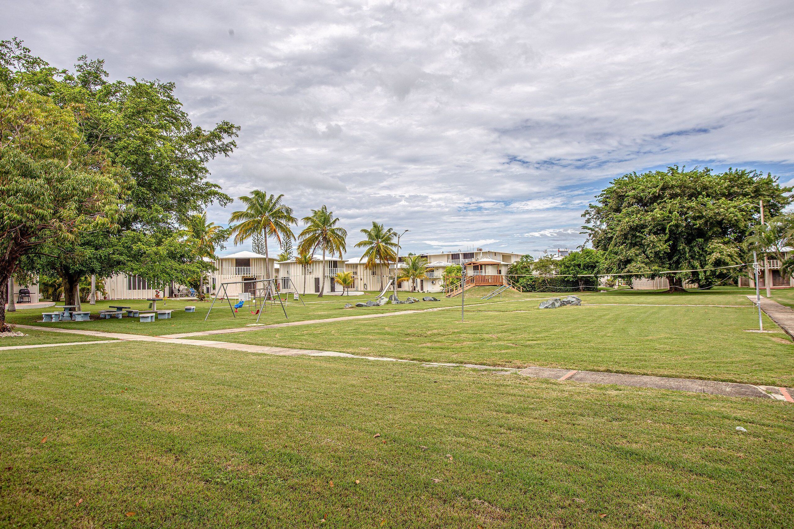 A grassy area with picnic tables, a playground, and a building with a staircase.