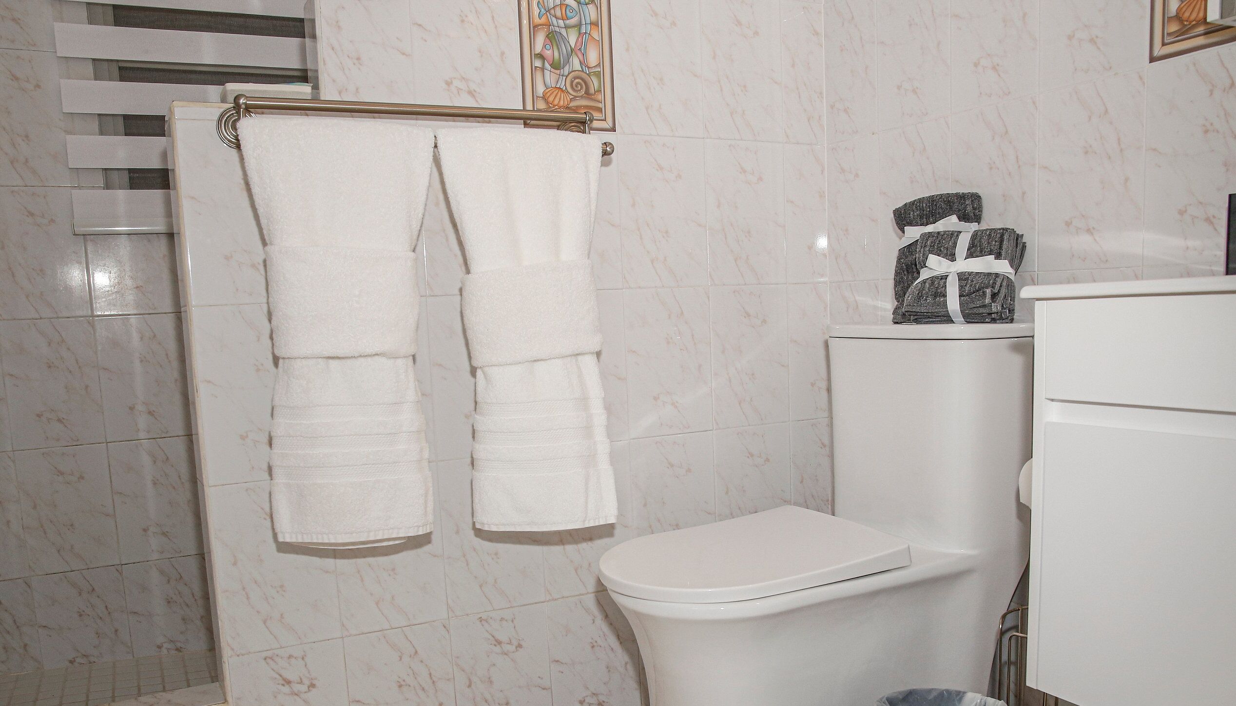 Un baño con un inodoro, un perchero con dos toallas y un adorno sobre el tanque del inodoro.