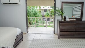 A bedroom with a bed, a dresser, and a balcony with a view of greenery and a building. -  EcoMar Rentals Villa (Cabo Rojo)