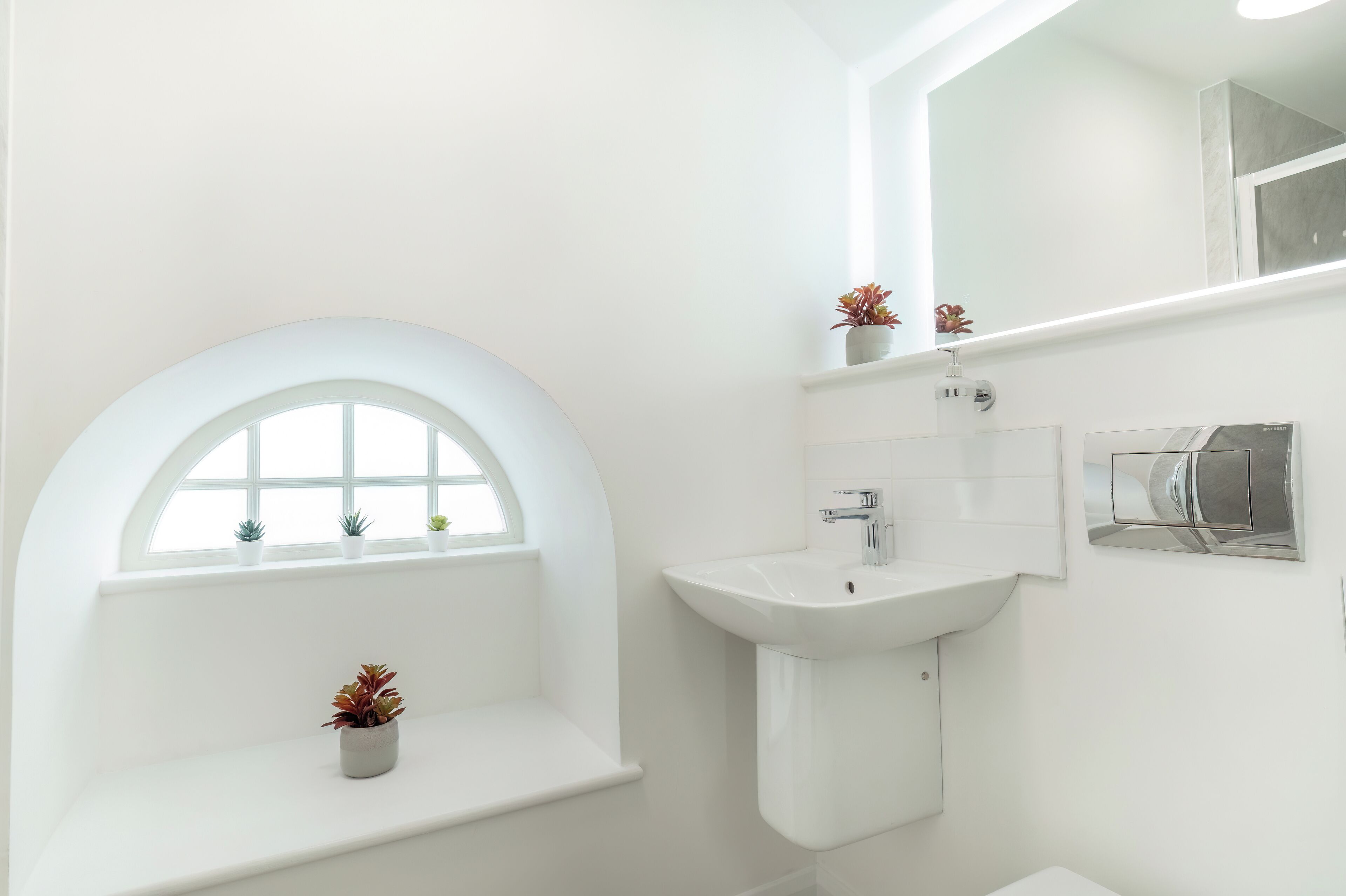 A bathroom with a white sink, a mirror, and a window with plants.