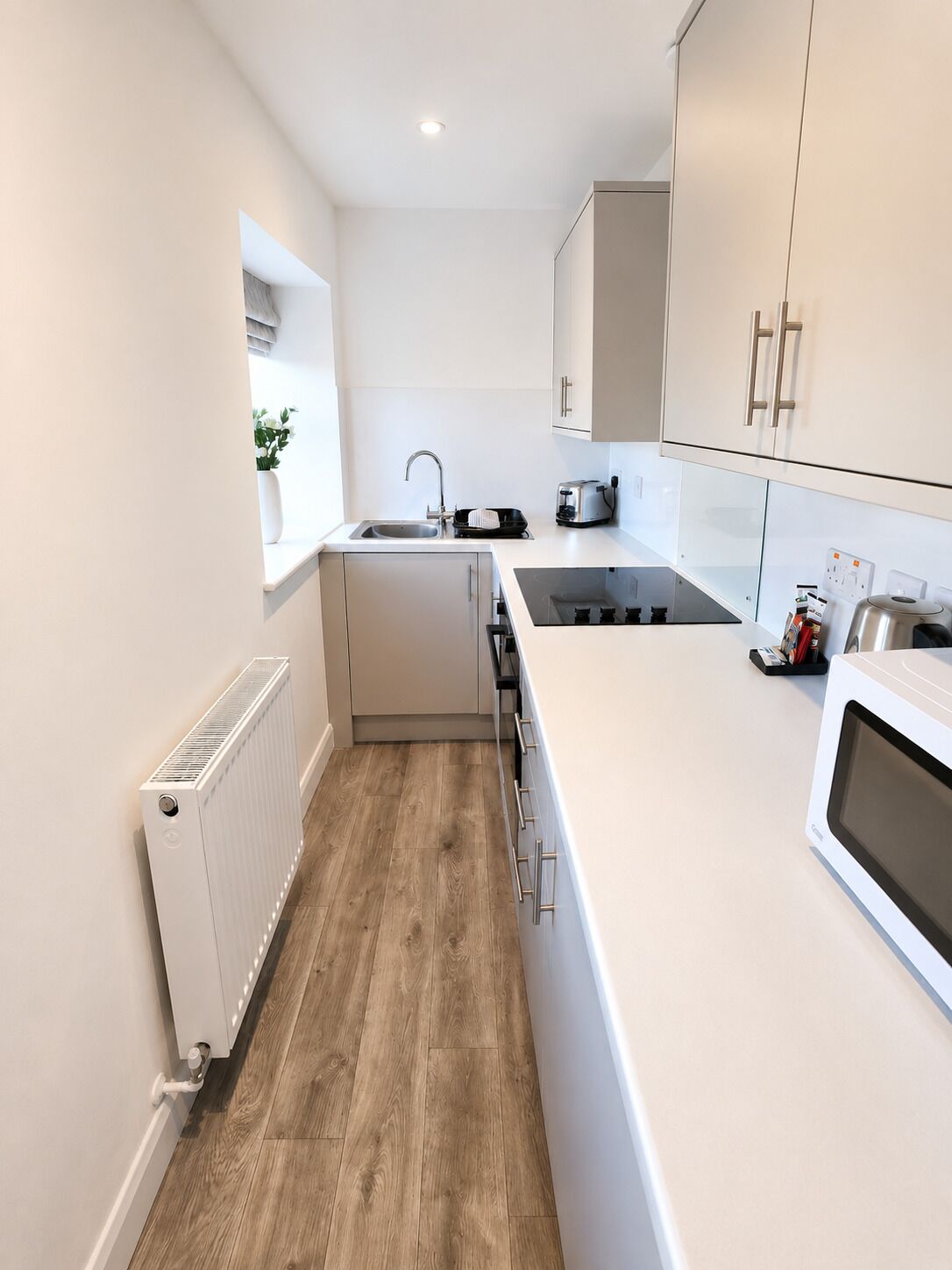 A modern kitchen with white cabinets, a built-in oven, a sink, and a window with a plant.