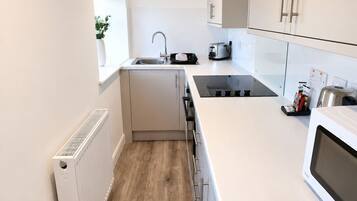 A modern kitchen with white cabinets, a built-in oven, a sink, and a window with a plant.