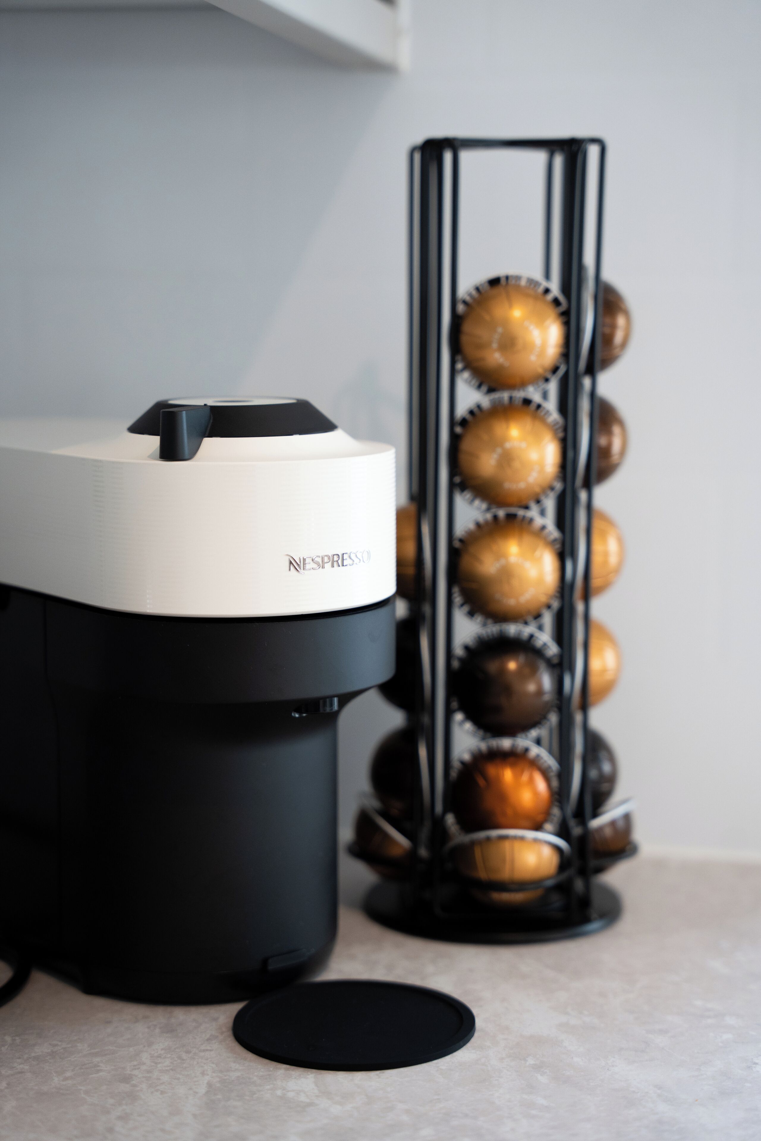 A Nespresso coffee machine with a black and white design, a coffee pod holder with multiple pods, and a black circular base.