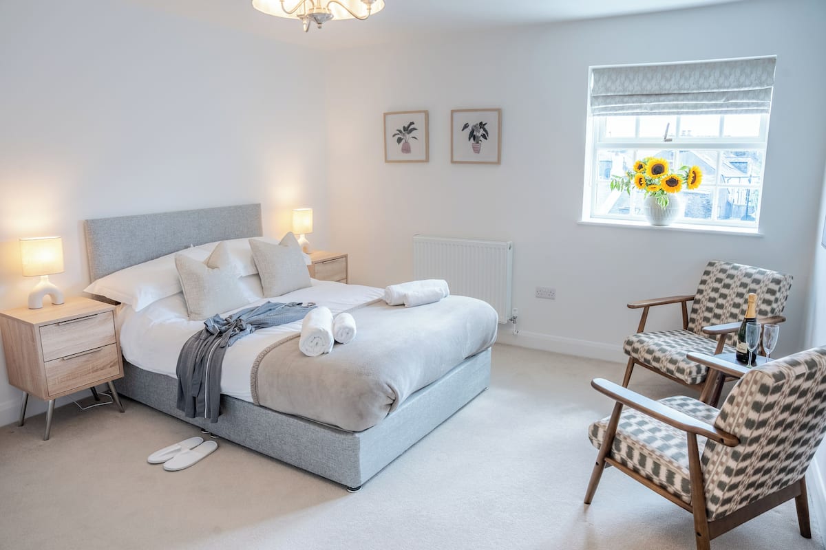 Une chambre à coucher comprenant un lit, des tables de chevet, une chaise, un radiateur et une fenêtre donnant sur un paysage agréable.