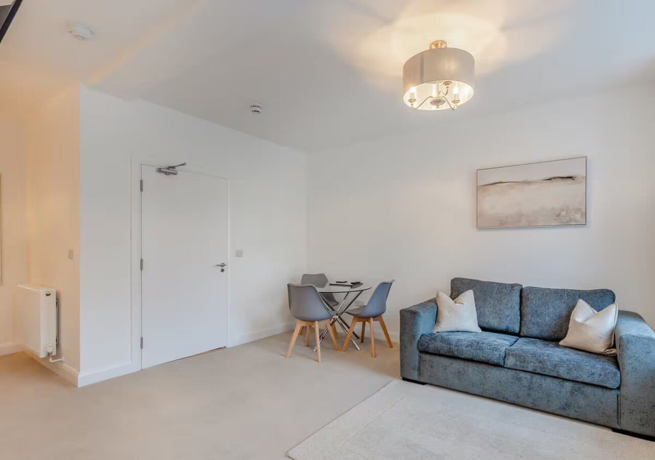 Un salon moderne avec un canapé gris, une table à manger avec des chaises, une porte blanche et un luminaire au plafond.