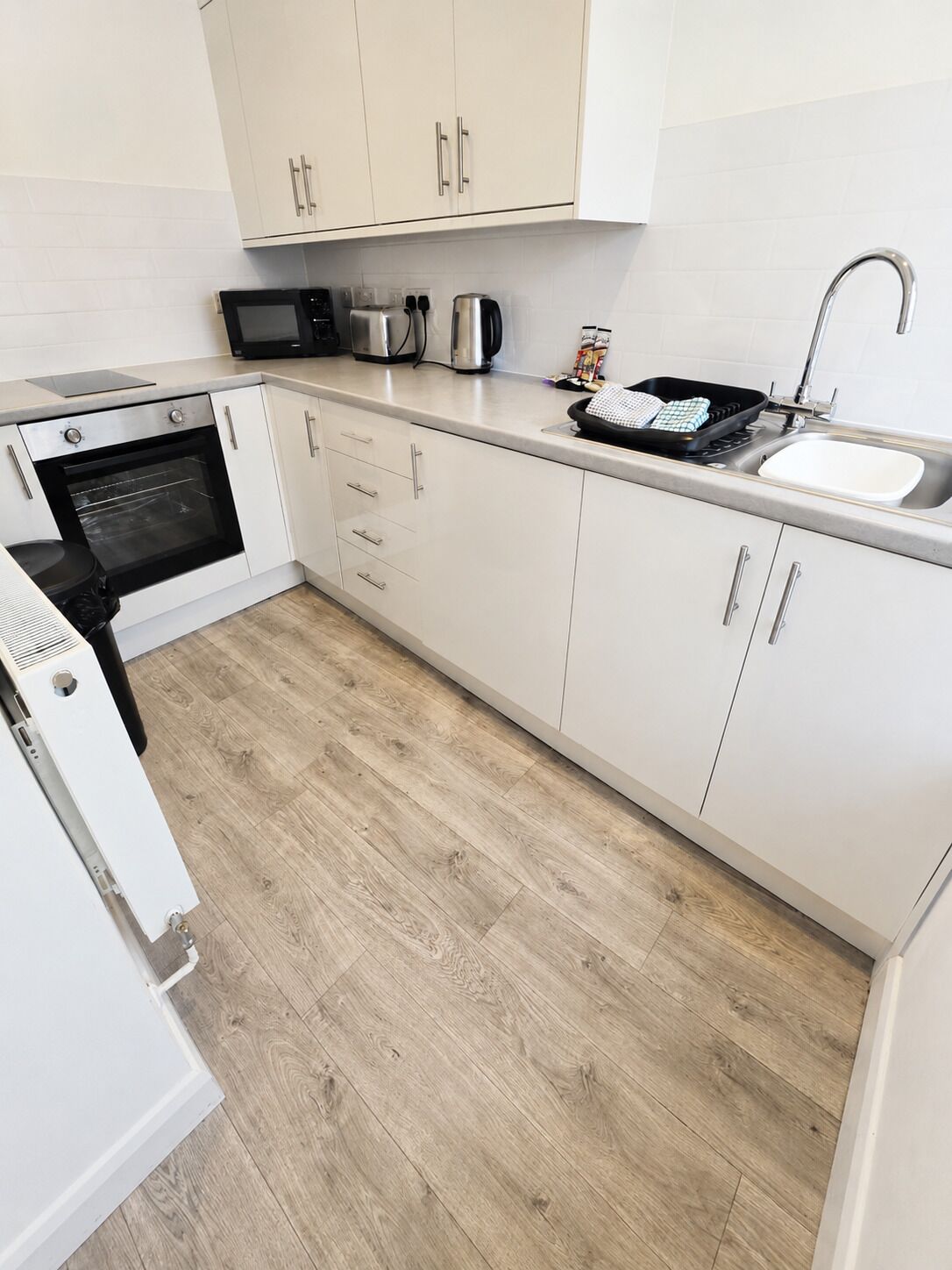 A modern kitchen with white cabinets, a microwave, a kettle, and a sink.