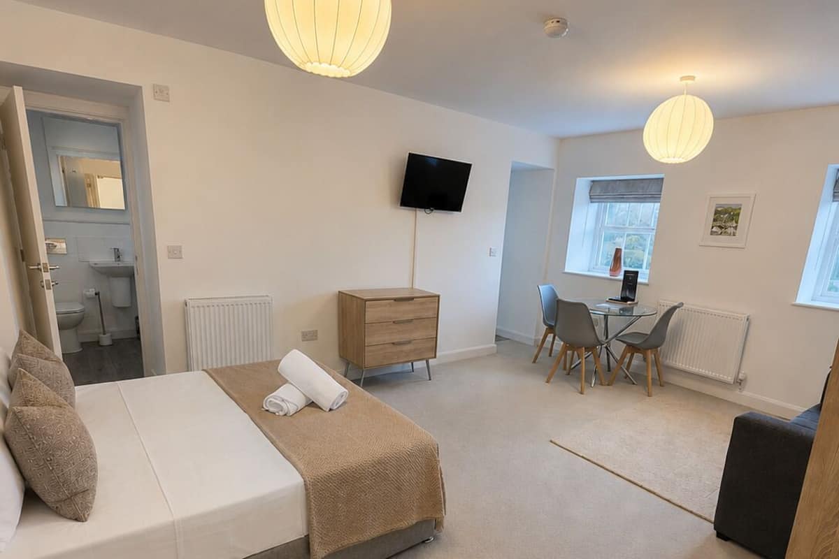 Une chambre à coucher comprenant un lit, une table de chevet, une commode, une télévision, ainsi qu’un coin repas avec des chaises et une table.