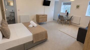 A bedroom with a bed, bedside table, dresser, TV, and a dining area with chairs and a table.