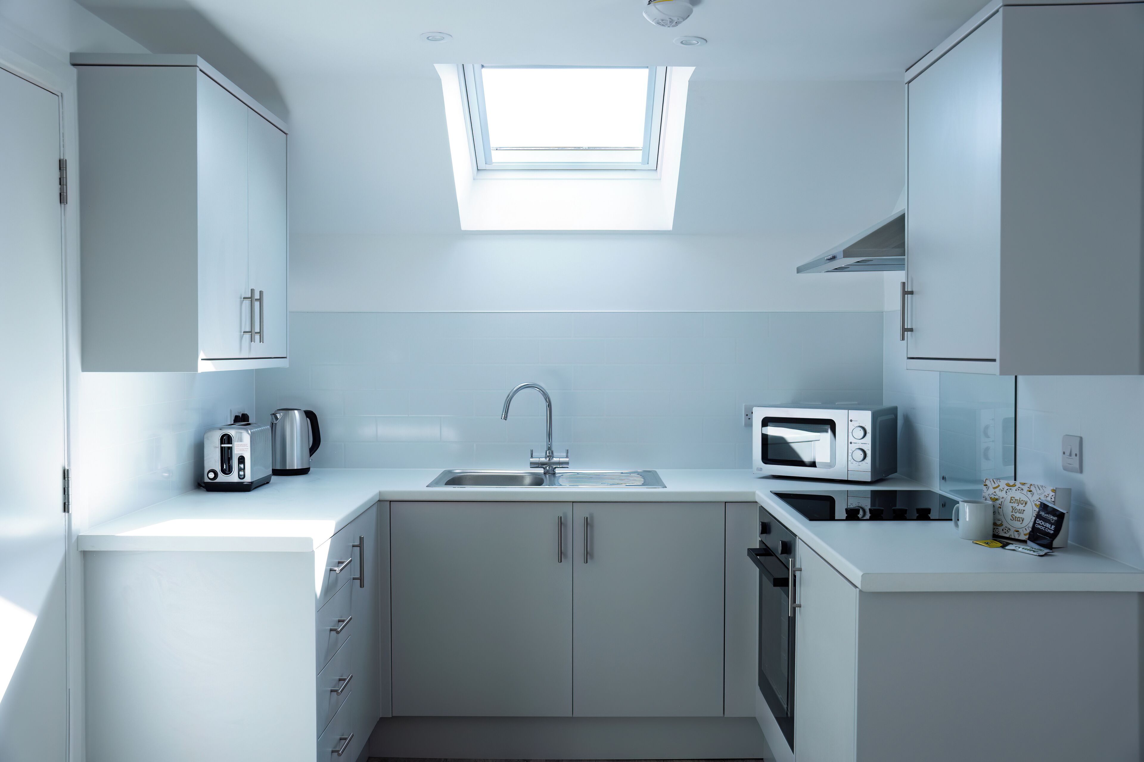 Een moderne keuken met witte kasten, een dakraam, een gootsteen, een broodrooster, een waterkoker en een magnetron.