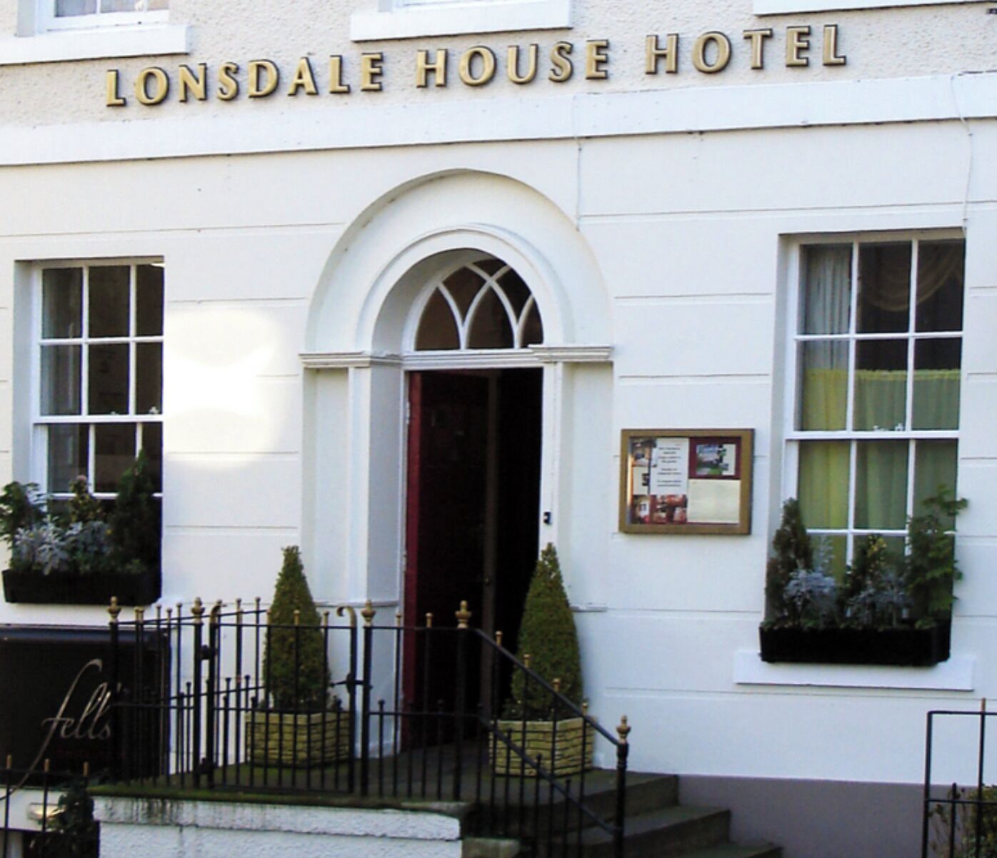 The exterior of Lonsdale House Hotel with a prominent arched entrance, a signboard above the entrance, and a small notice board on the wall.