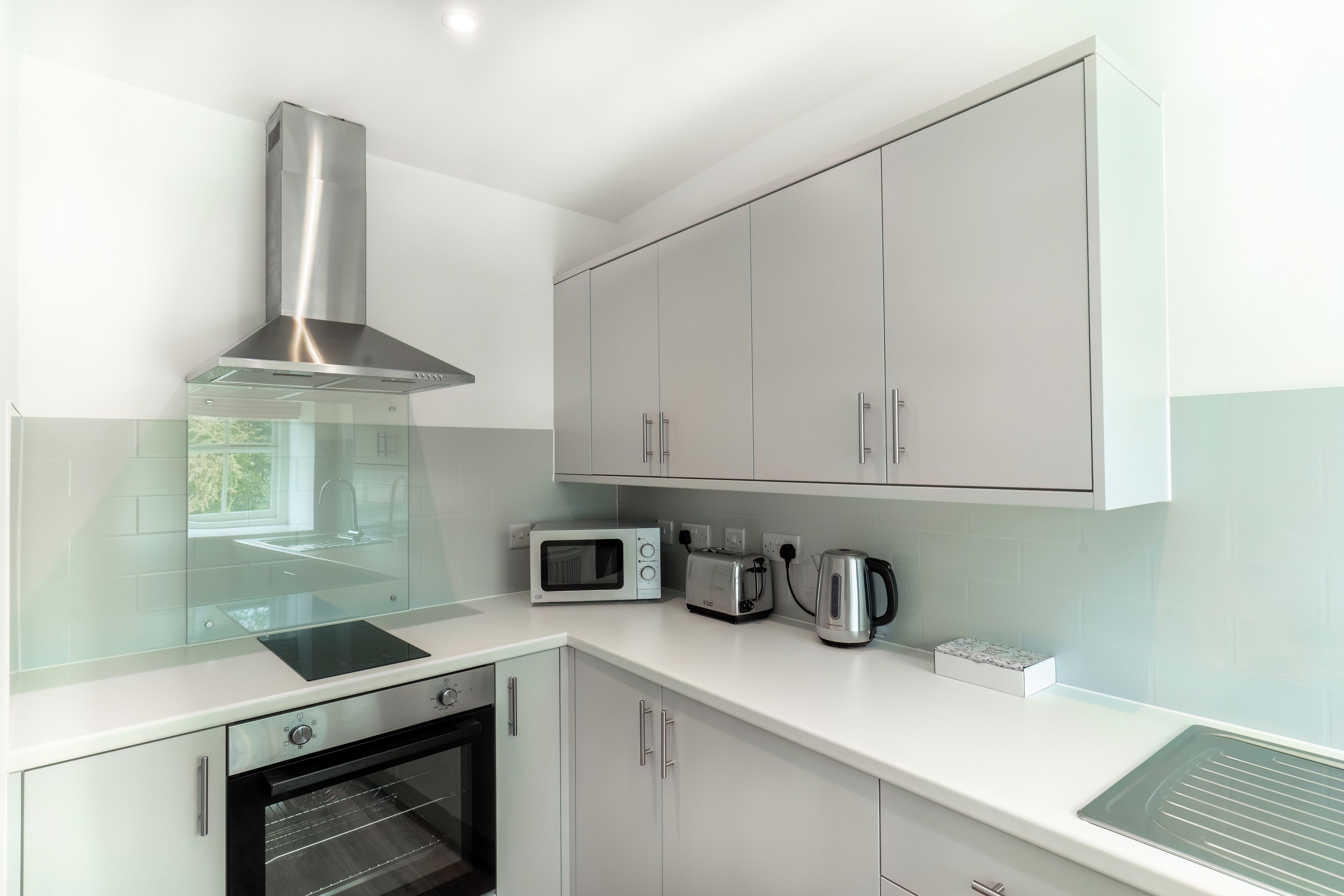 Una cocina moderna con armarios blancos, una campana extractora de acero inoxidable, un microondas, un tostador y un hervidor.