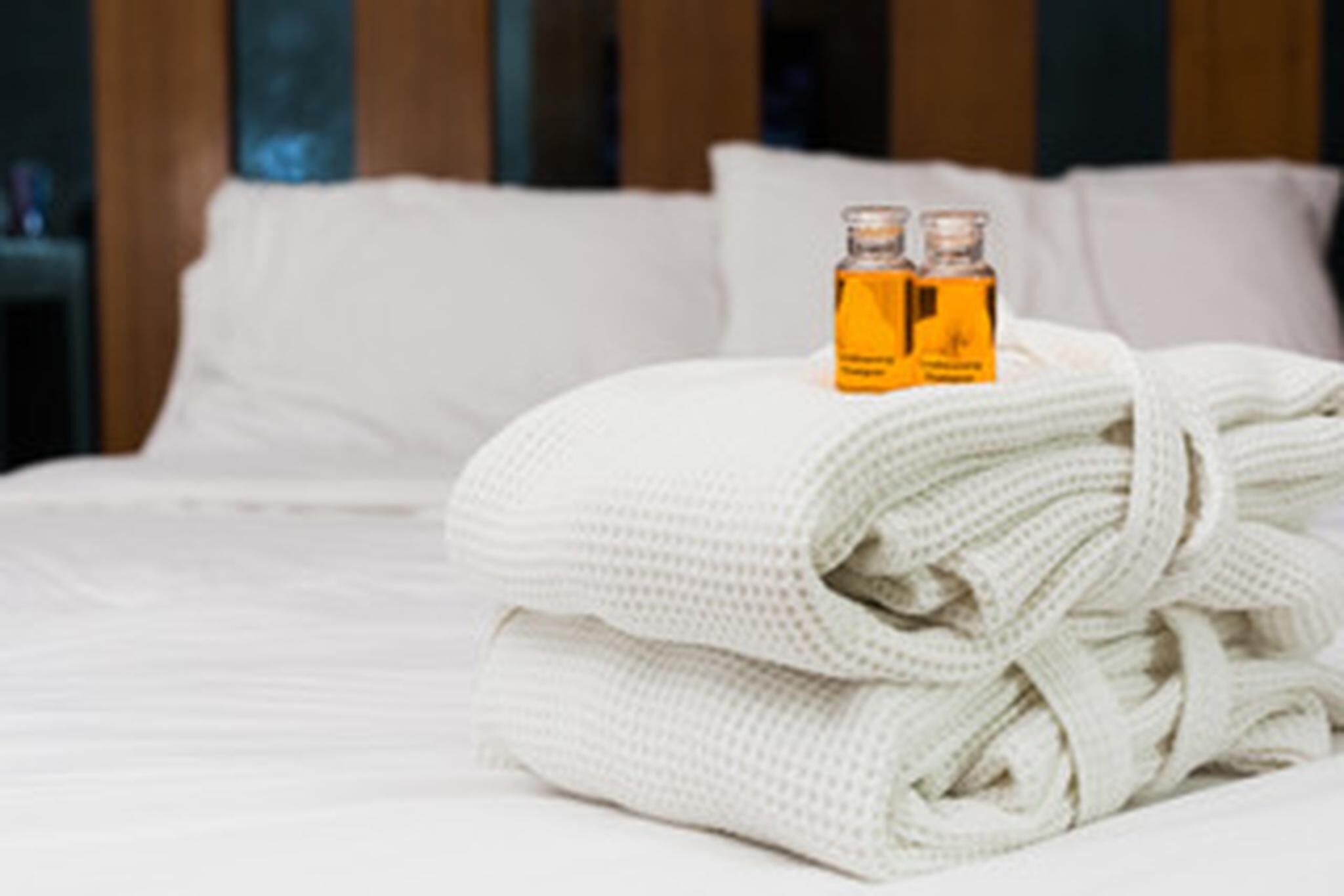 A neatly made bed with a folded white towel and two bottles of lotion on top.
