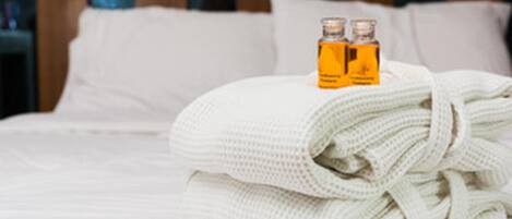 A neatly made bed with a folded white towel and two bottles of lotion on top.