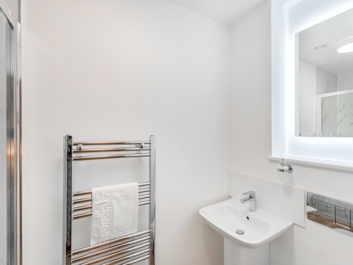 Une salle de bain moderne avec un porte-serviettes chromé, un lavabo blanc et un miroir au-dessus.