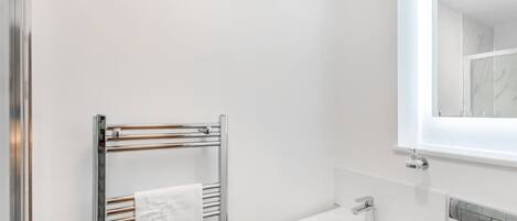 Une salle de bain moderne avec un porte-serviettes chromé, un lavabo blanc et un miroir au-dessus.