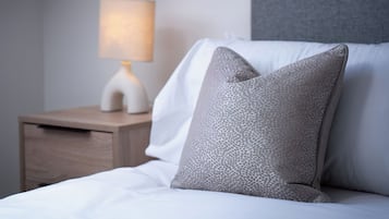 A neatly made bed with white linens and two grey pillows, a bedside table with a lamp, and a grey headboard.
