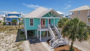 A beachfront house with a balcony, a staircase leading to the entrance, and a flag. - Super Cute!   Easy Beach & Pool Access (Gulf Shores)