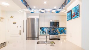 A modern kitchen with a central island, stainless steel appliances, and a blue hexagonal tile backsplash.