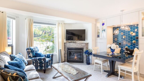 A modern living room with a fireplace, a dining area, and a kitchen with a blue hexagonal backsplash.