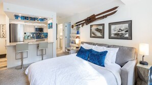 A modern hotel room with a large bed, a kitchenette, and a view of the mountains.