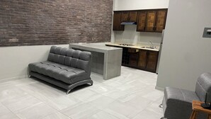 A modern kitchen with a grey sofa and ottoman, a brick wall, and wooden cabinets. - AB Bed and breakfast  (Chihuahua)
