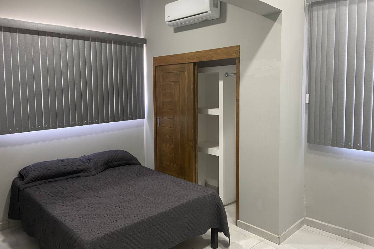A bedroom with a bed, a wardrobe, and an air conditioning unit.