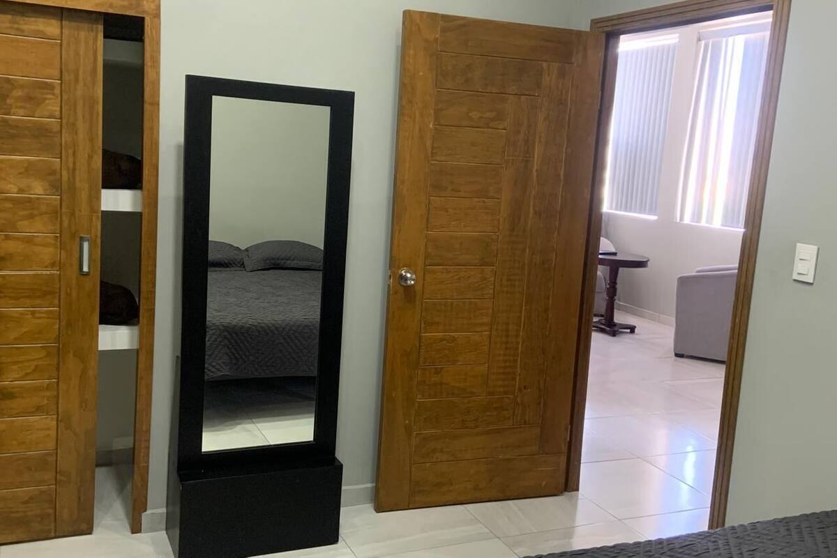 A room with a large mirror, wooden doors, and a bed with a gray bedspread.