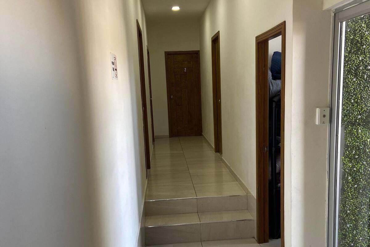 A hallway with a tiled floor, a wooden door at the end, and a window with a view of greenery.