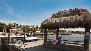 Un muelle con una estructura de techo de paja, bancos y vistas al agua y palmeras.
