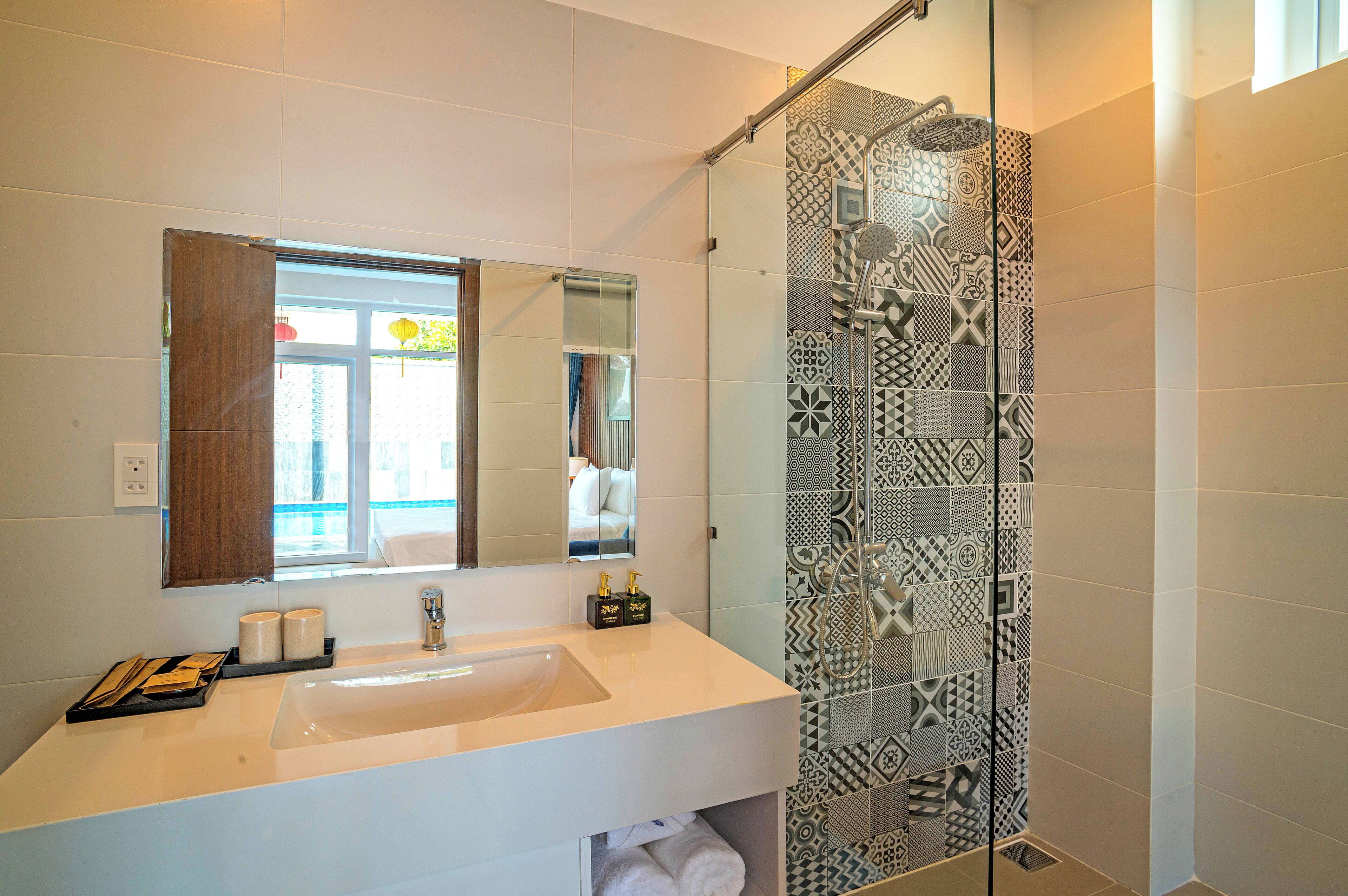 A modern bathroom with a large mirror, a white sink, and a shower with patterned tiles.
