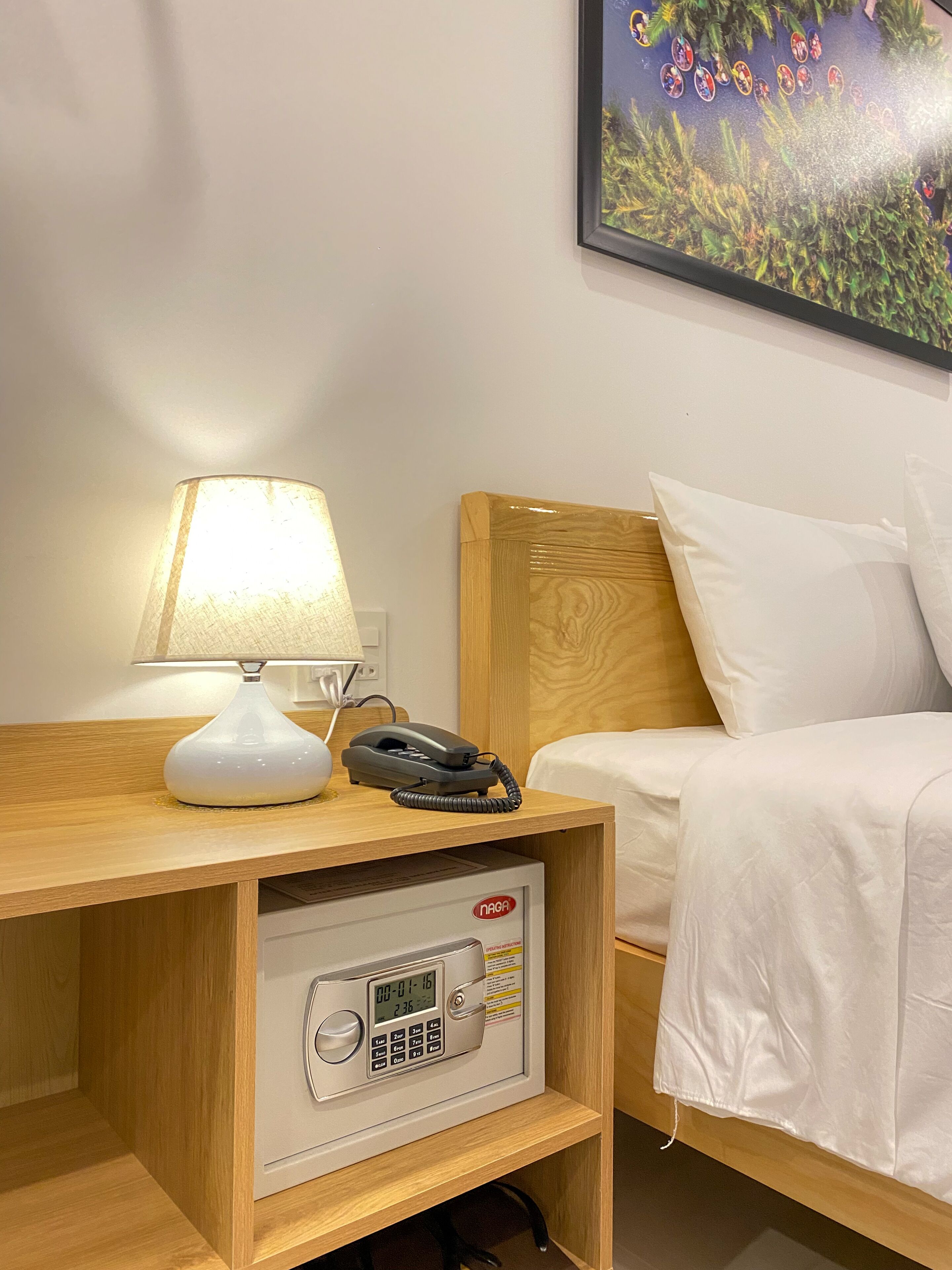 A hotel room with a wooden nightstand, a white lamp, a telephone, and a safe.