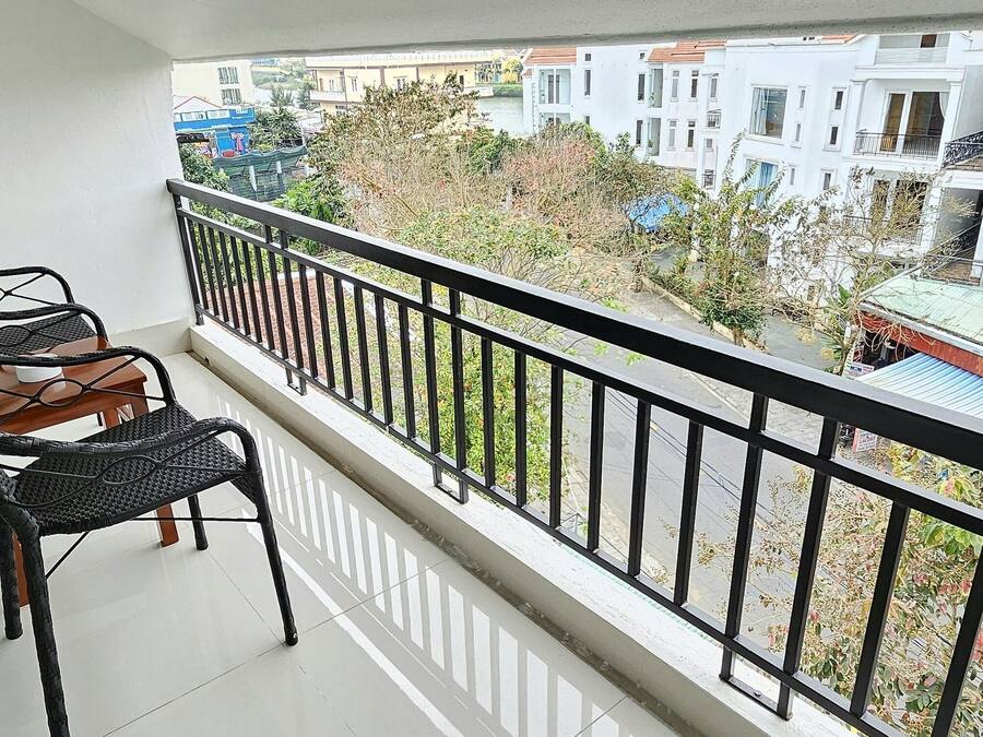 Een balkon met twee rieten stoelen en een kleine tafel, met uitzicht op een woonwijk met meerlaagsgebouwen.