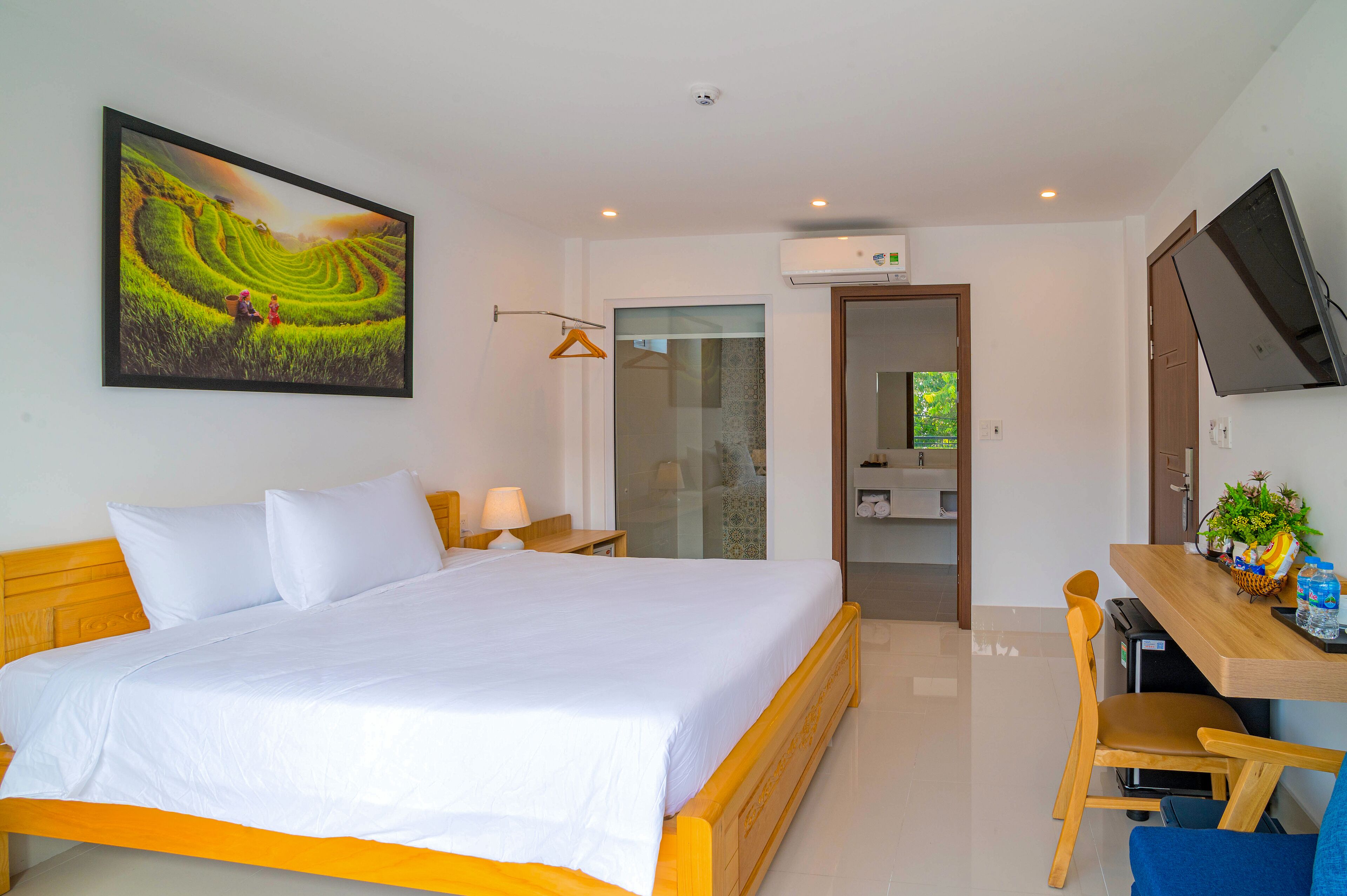 A hotel room with a large bed, a desk with a chair, a television, and a painting on the wall.