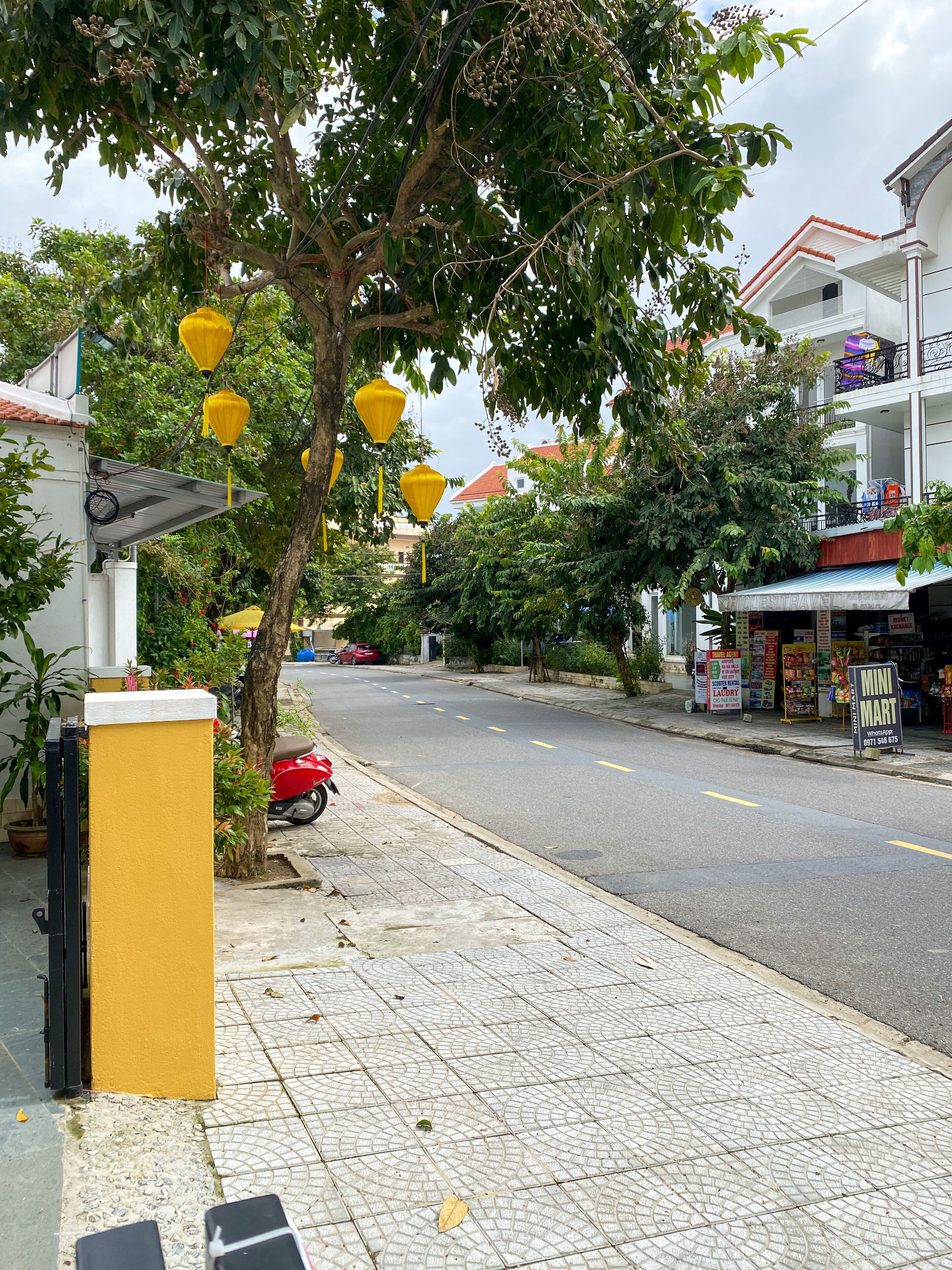 A street with yellow lanterns, a red motorcycle, and a Mini Mart store.