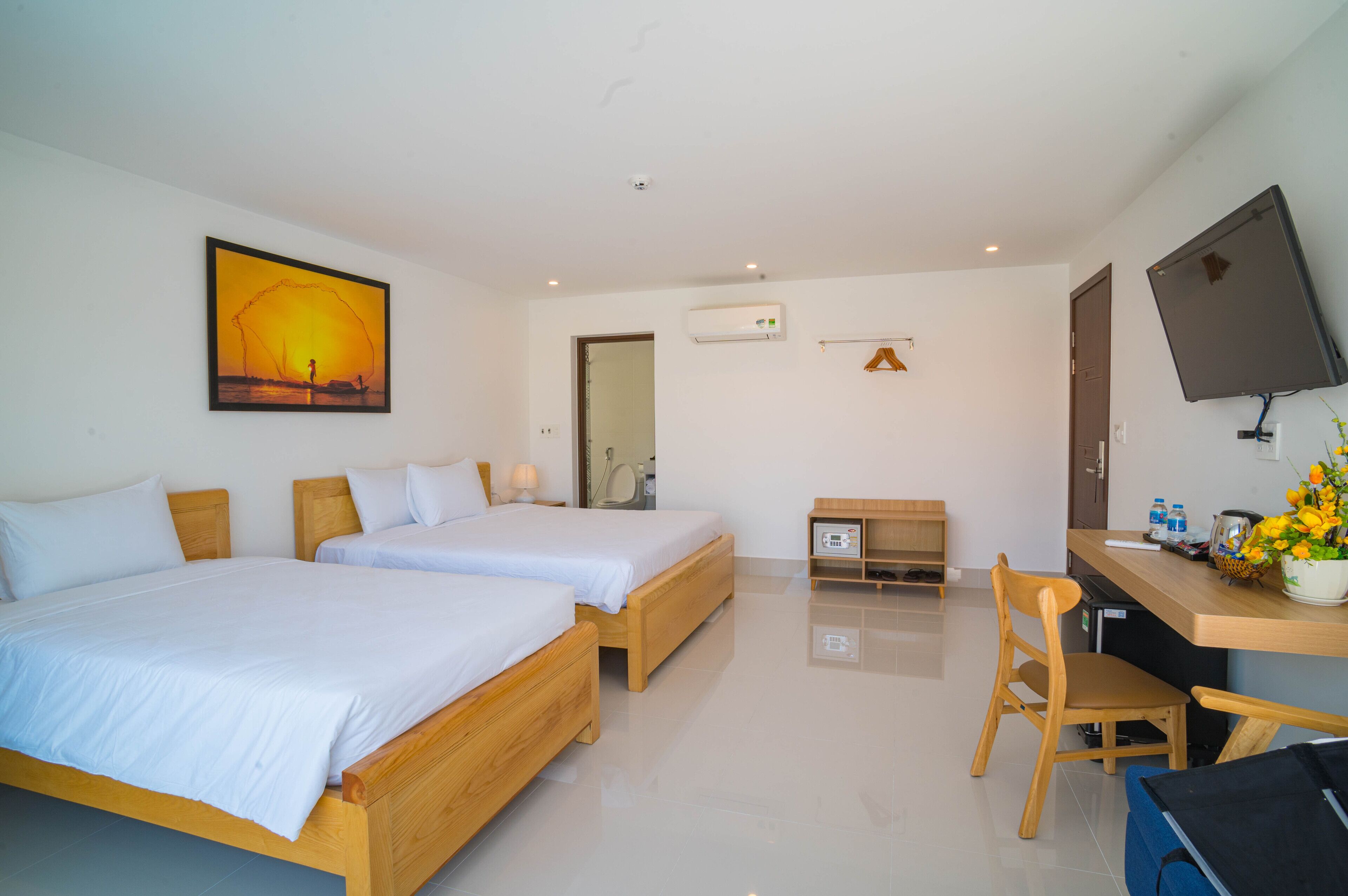 A hotel room with two wooden beds, a desk with a chair, a flat-screen TV, and a painting on the wall.