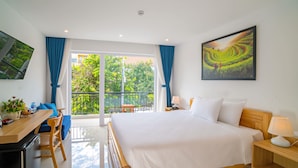 Et hotelværelse med en stor seng, et skrivebord med stol, en balkon med bord og stole, og et billede på væggen.