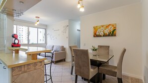 Eine moderne Küche mit Holzarbeitsplatte, ein Essbereich mit Tisch und Stühlen sowie ein Wohnbereich mit Sofa und einem Gemälde an der Wand.