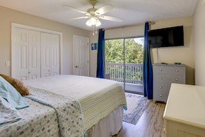 A bedroom with a bed, a ceiling fan, a TV, a dresser, and a balcony with a view of trees. - Charming PCB Condo w/ Balcony: Walk to Beach! (Panama City Beach)