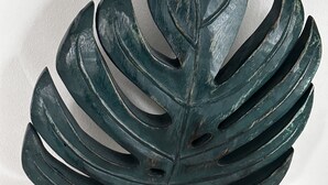 A dark green, leaf-shaped sculpture on a black stand.