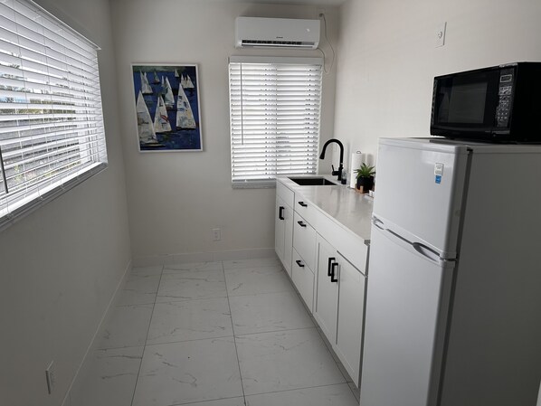 Una cocina con armarios blancos, un refrigerador blanco, un microondas, un lavaplatos y un cuadro de veleros.