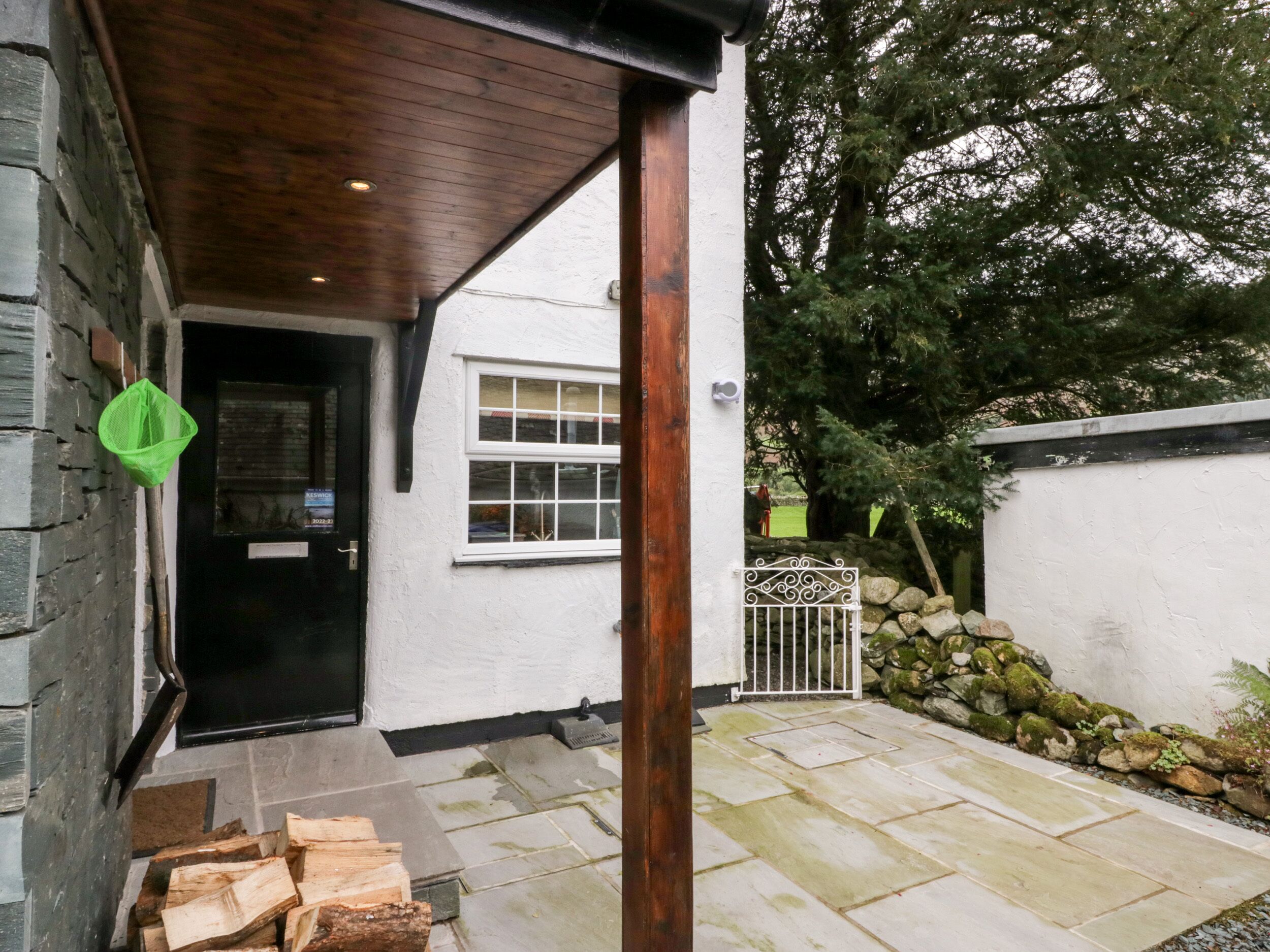A stone building with a black door and a window, a wooden door frame, and a pile of firewood outside.
